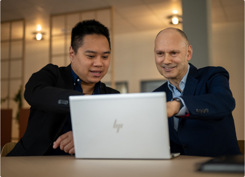 Zwei Männer arbeiten an einem Tisch an einem Laptop zusammen und betreiben Karrierecoaching vor einem sanft beleuchteten Hintergrund.